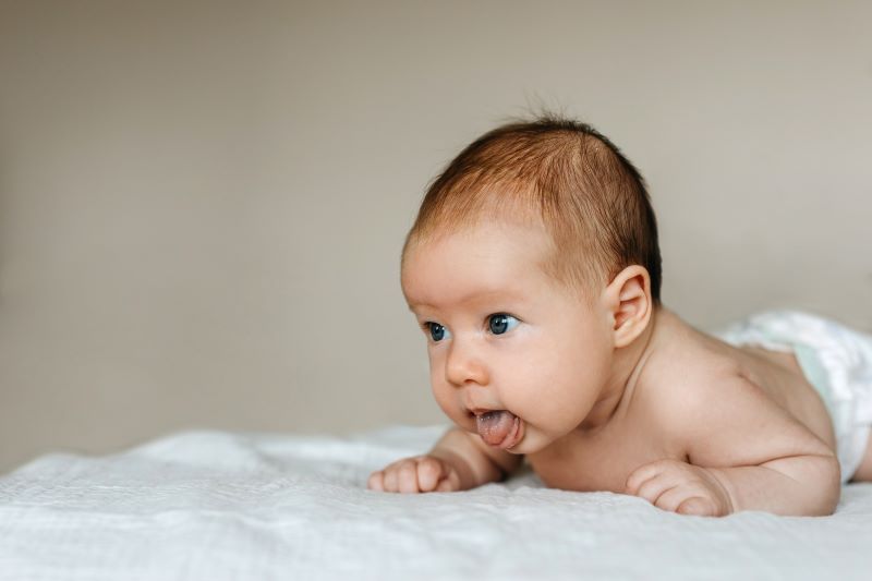Infant lying on their belly, sticking their tongue out